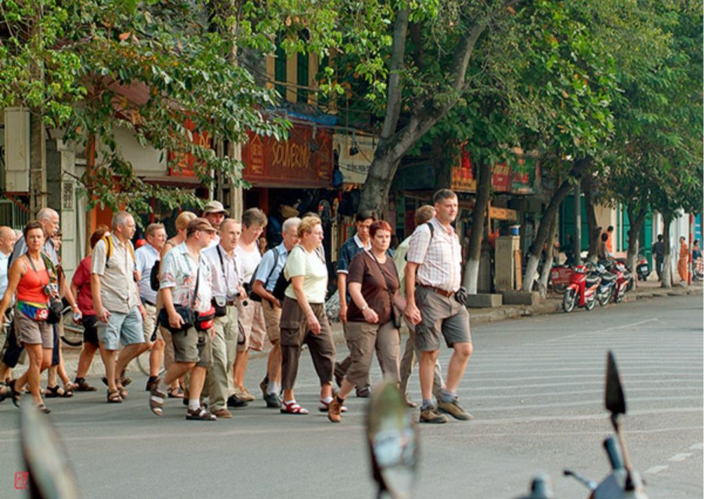 A large group of western tourists walking through the sunny streets of Hanoi Old Quarter during the dry season