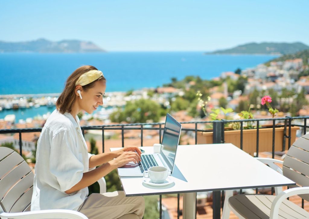 Woman working on laptop at a cafe with a scenic sea view