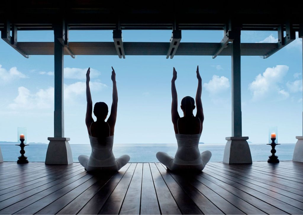 Silhouettes of two women practicing yoga facing the ocean.